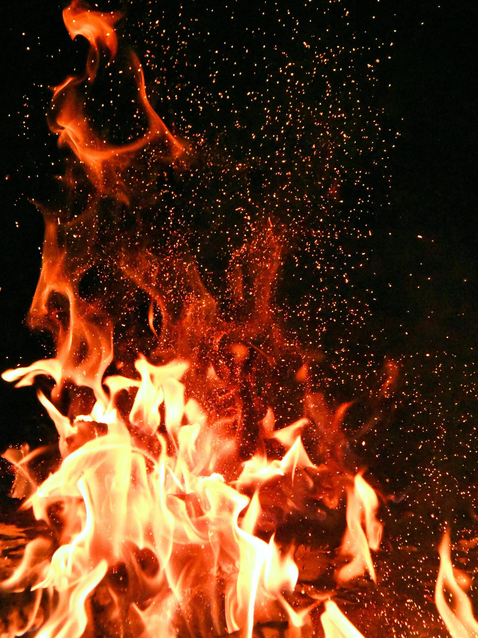 Vivid orange flames and sparks dance against a mysterious black backdrop.